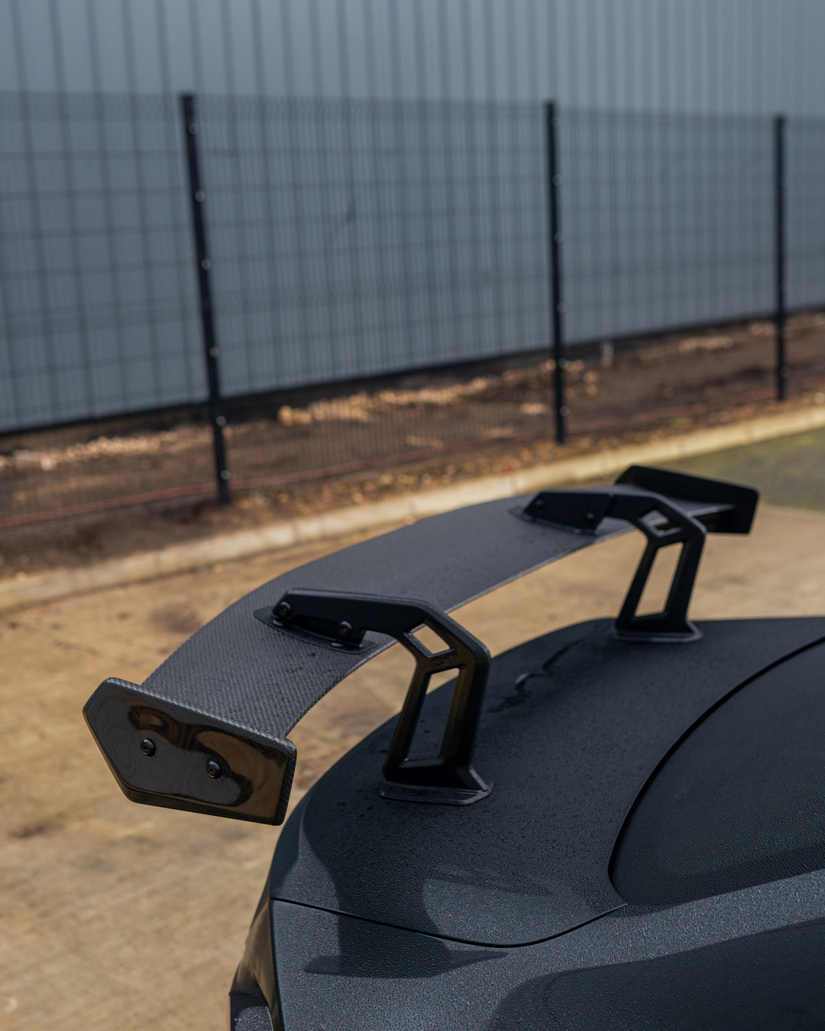 BMW G87 M2 and G42 2 Series carbon fibre swan neck wing spoiler by CT Design, shown on a sleek sports car.
