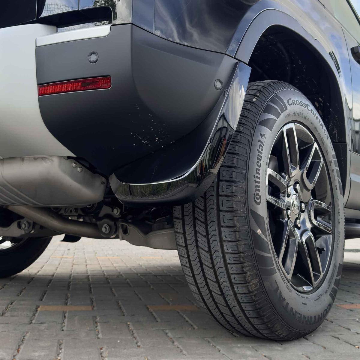Gloss black mud flaps for Land Rover Defender L663 110 and 90, by CT Carbon, installed on the vehicle's wheel arches.