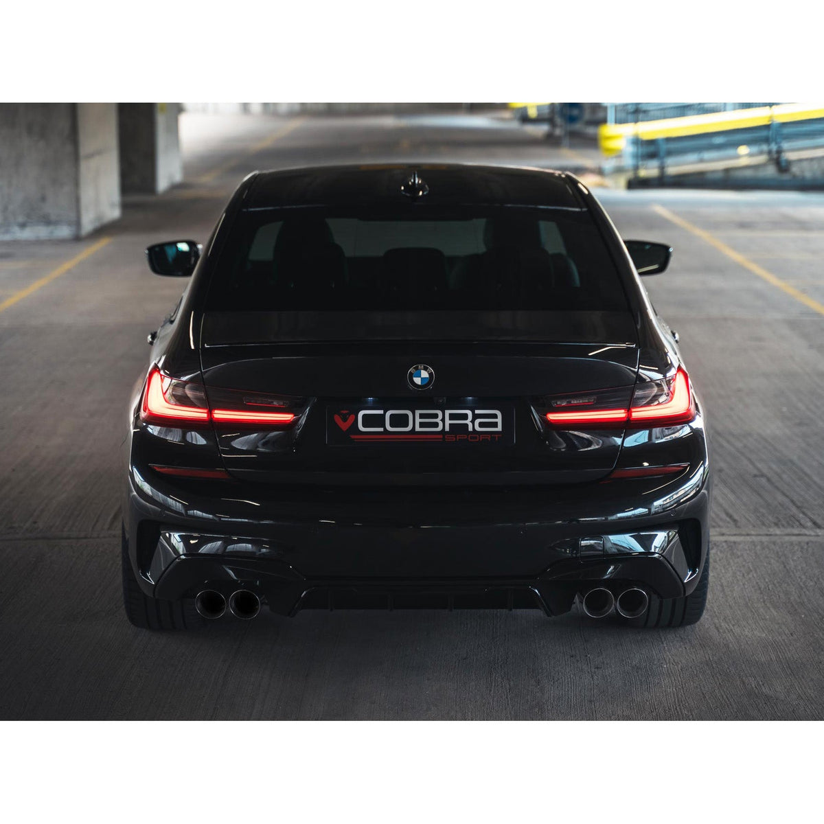 Cobra Sport BMW 320i G20 quad exit exhaust conversion with M3 style non-valved quad tips on a black car.