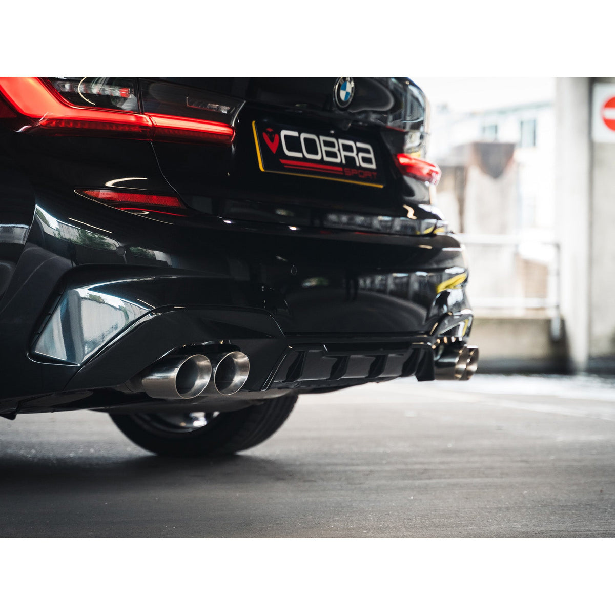 Cobra Sport BMW 320i G20 non-valved quad exit M3 style performance exhaust installed on a car in a lifestyle setting.