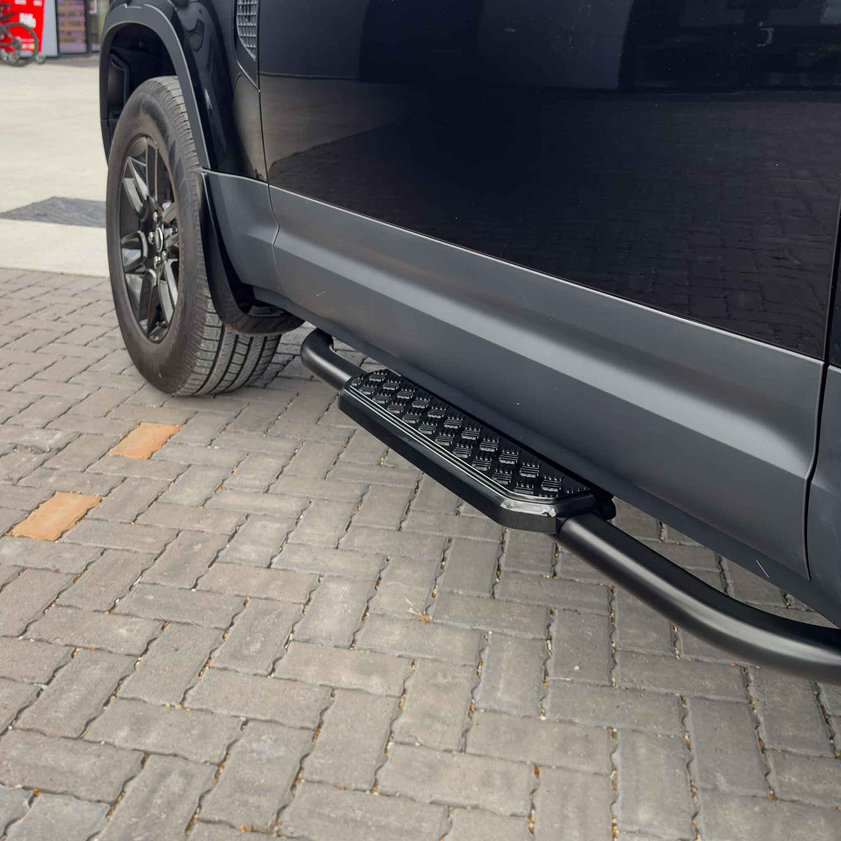 Land Rover Defender L663 90 side steps by CT Carbon, black metal accessories mounted along the sides of the vehicle.
